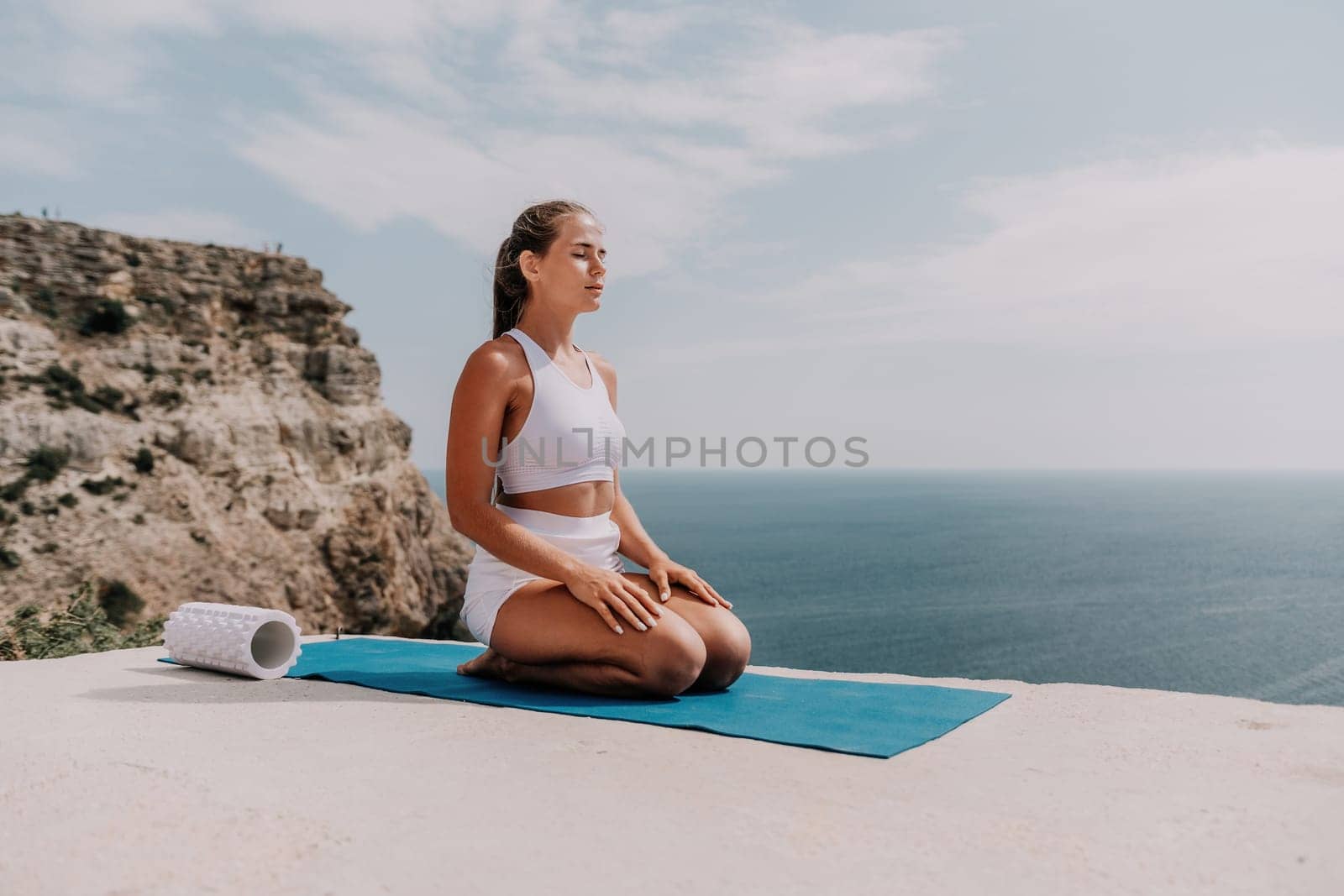 Middle aged well looking woman with black hair doing Pilates with the ring on the yoga mat near the sea on the pebble beach. Female fitness yoga concept. Healthy lifestyle, harmony and meditation.