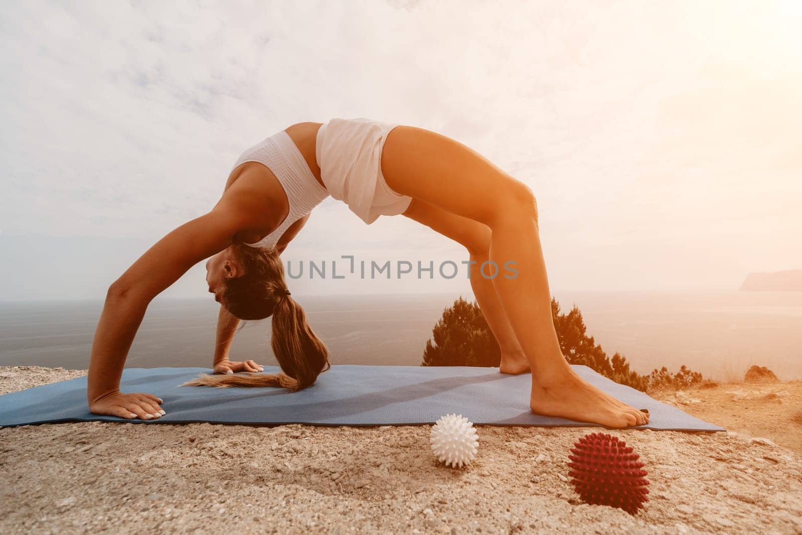 Middle aged well looking woman with black hair doing Pilates with the ring on the yoga mat near the sea on the pebble beach. Female fitness yoga concept. Healthy lifestyle, harmony and meditation.