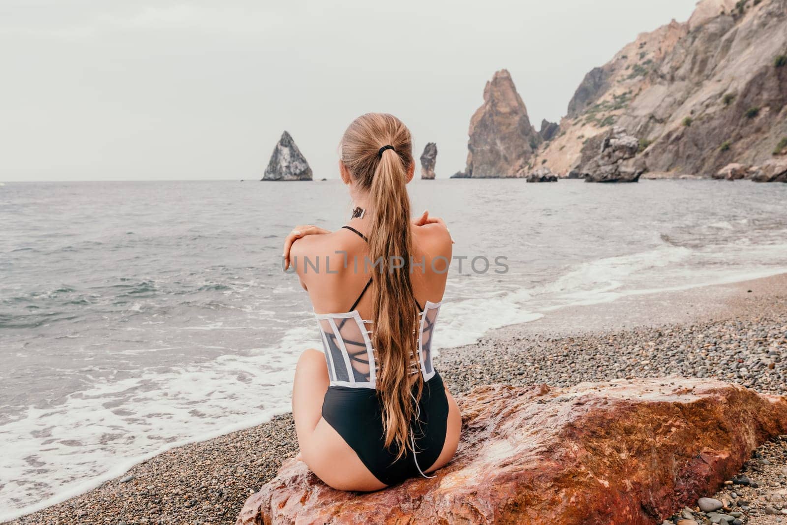 Side view a Young beautiful sensual woman in a mint long dress posing on a volcanic rock high above the sea during sunset. Girl on the nature on overcast sky background. Fashion photo