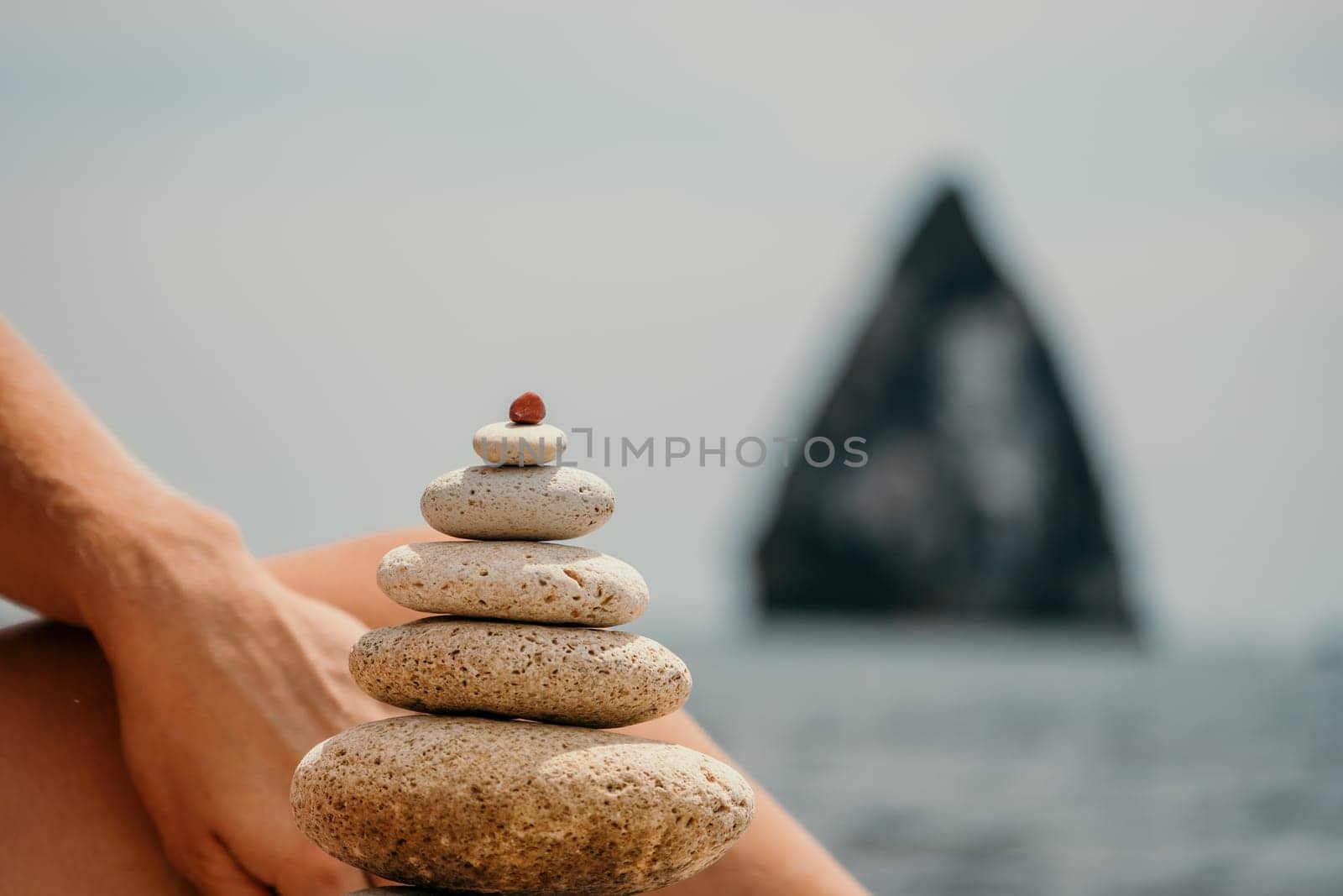 Woman bilds stones pyramid on the seashore on a sunny day on the blue sea background. Happy holidays. Pebble beach, calm sea, travel destination. Concept of happy vacation on the sea, meditation, spa