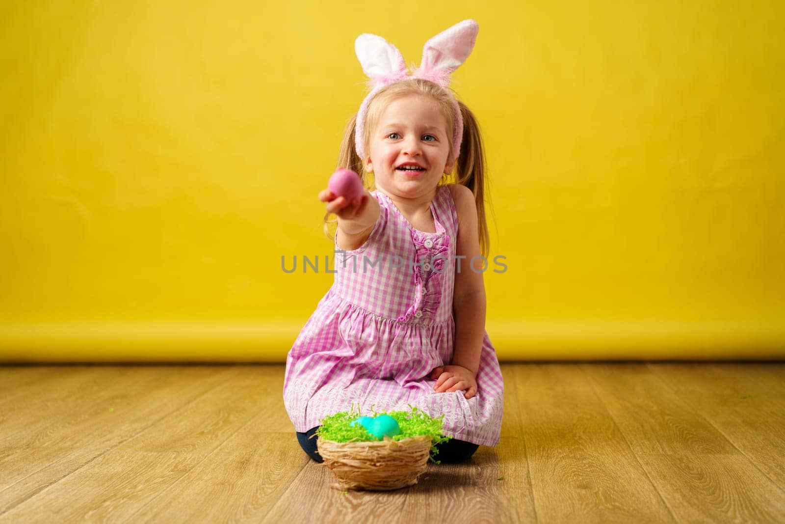 Toddler blonde happy girl with bunny ears and basket of eggs for Easter