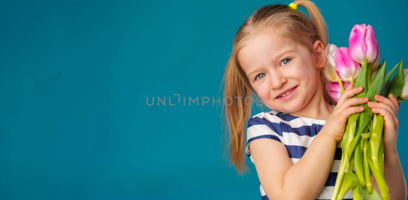 Smiling little blonde girl with tulips bouquet against blue background