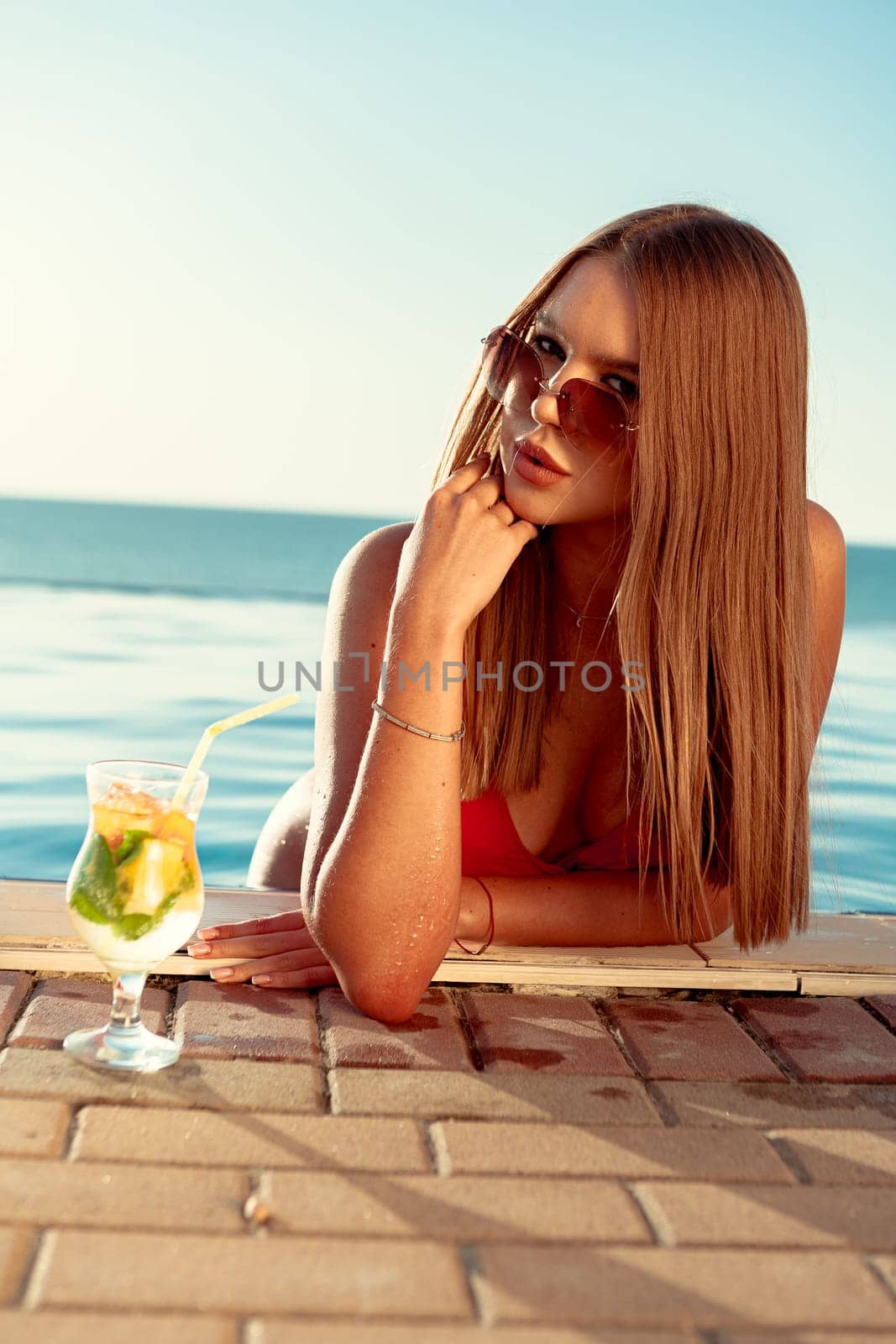 Tanned woman in red bikini in a pool with cocktail