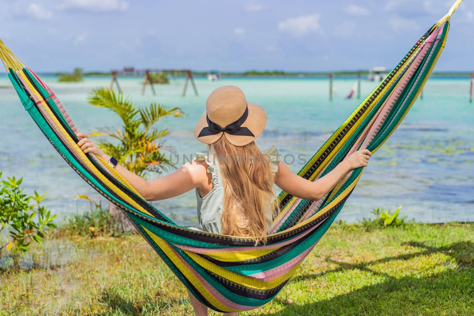 Female tourist sitting in hammock against background of turquoise waters of Lake Bacalar. Family bonding, summer vacation, and outdoor fun in Quintana Roo, Mexico concept.