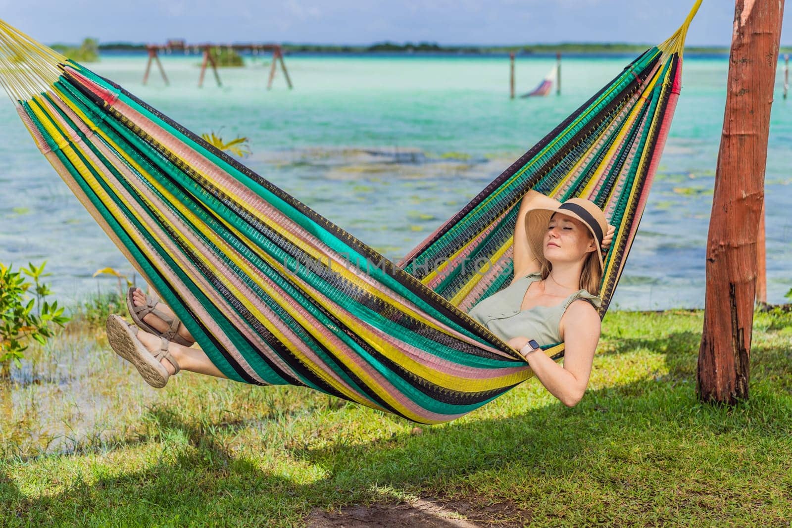 Female tourist sitting in hammock against background of turquoise waters of Lake Bacalar. Family bonding, summer vacation, and outdoor fun in Quintana Roo, Mexico concept.