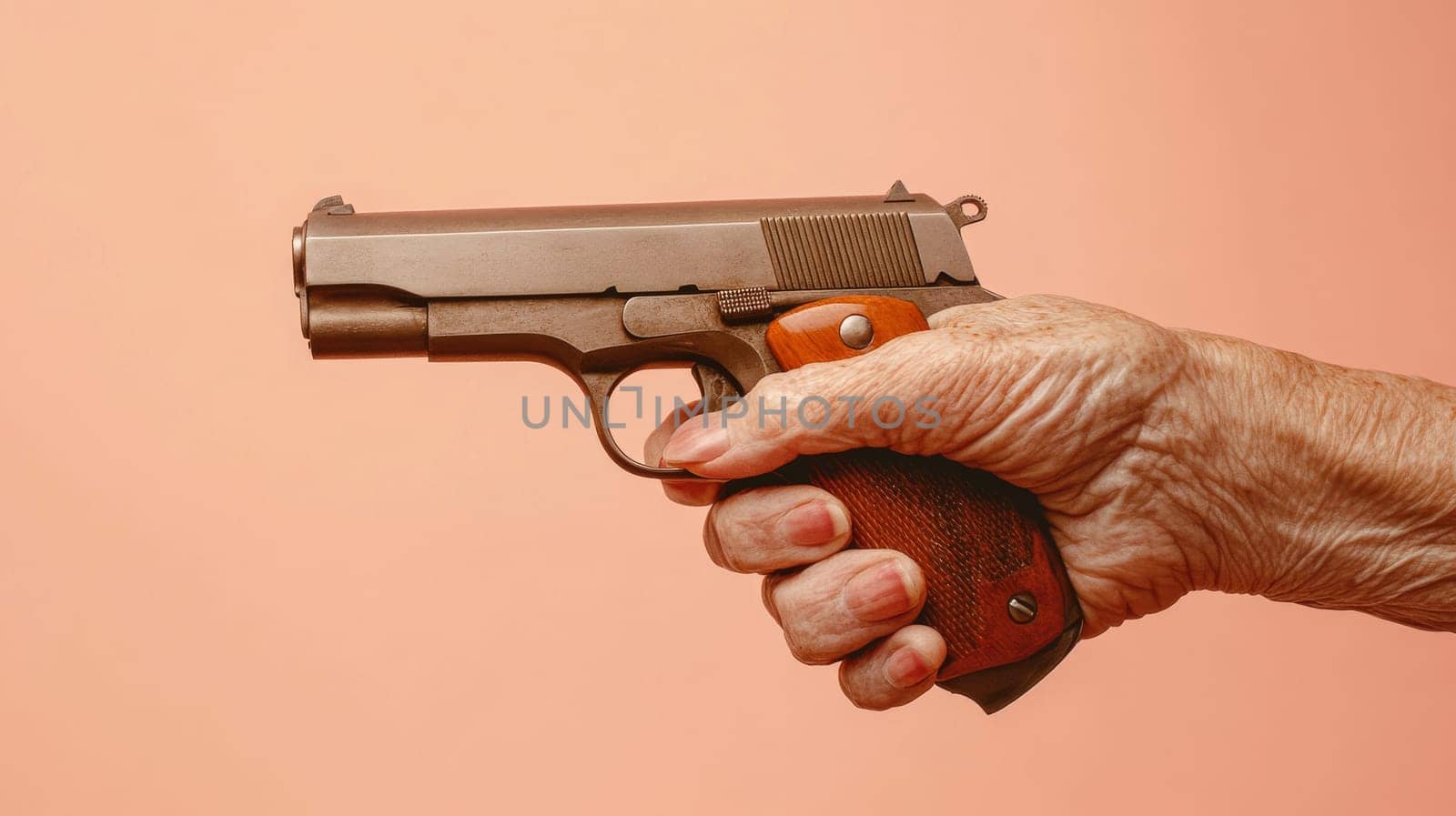 Elderly hand holding a handgun on peach background, safety and age concept.