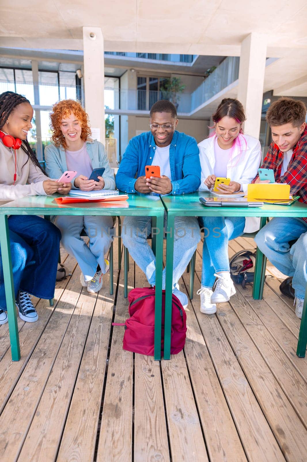 group of five happy students are studying outdoors at university, using smartphones. They're engaged, collaborating, and enjoying their learning experience in a modern, tech-friendly environment
