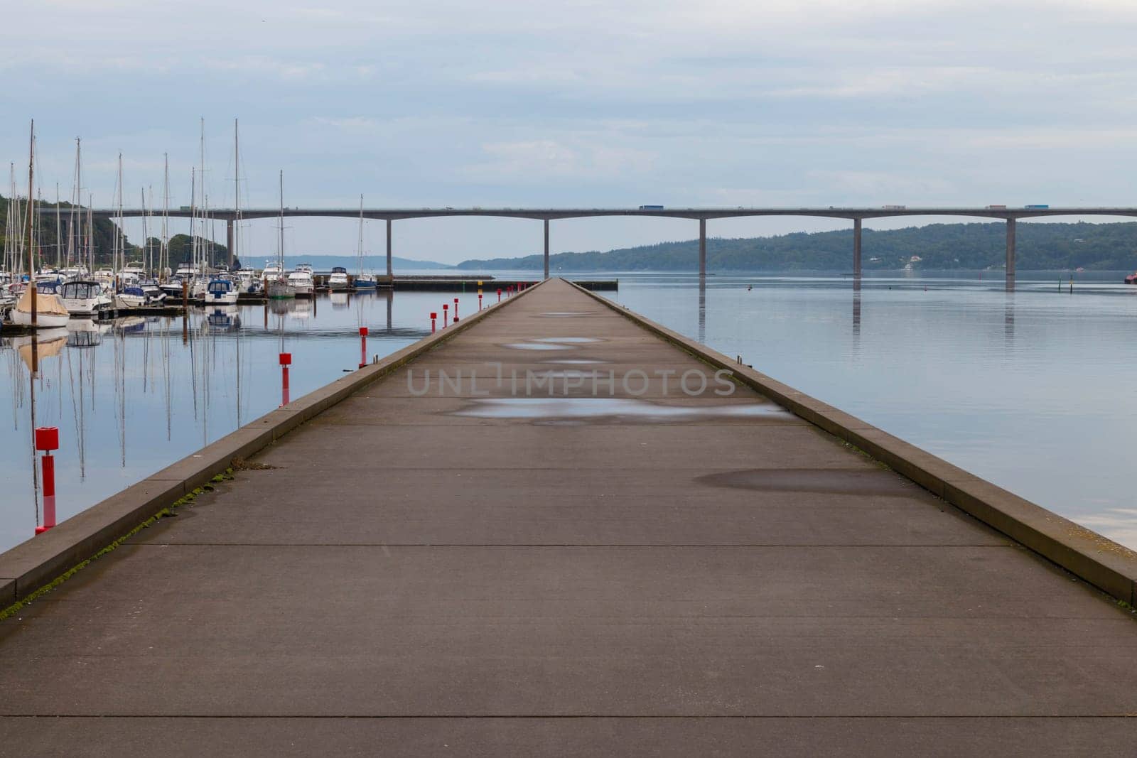 a wooden jetty or jetty in the water near vejle in denmark with the harbour and boats with a bridge in the background