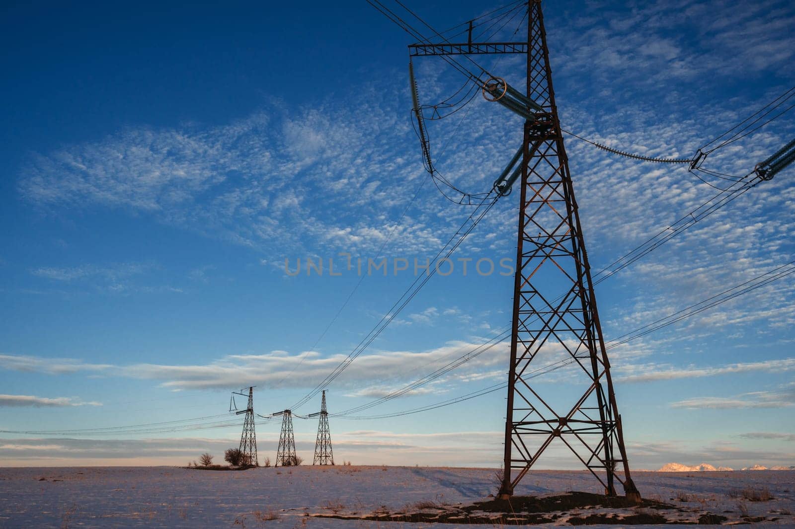 High-voltage power transmission line with towers in the field in winter at sunset in the evening