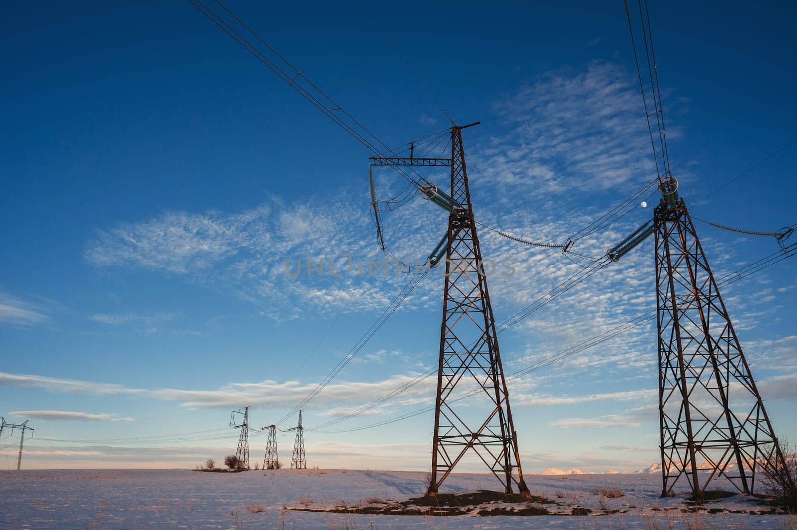 High-voltage power transmission line with towers in the field in winter at sunset in the evening