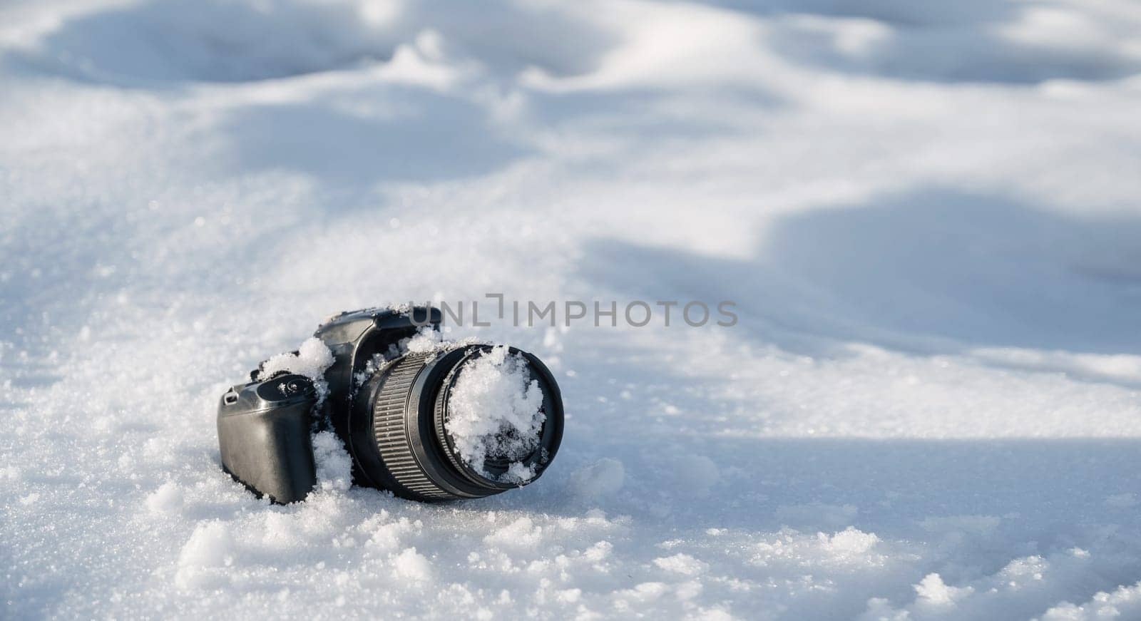 professional digital slr photo camera with frost lens lies in a snowdrift in winter in the snow with copy space