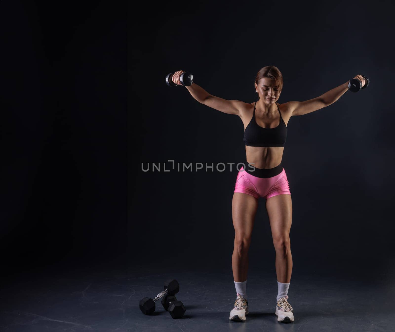 sporty girl doing exercises with dumbbells on black background, sport concept, healthy and beautiful body