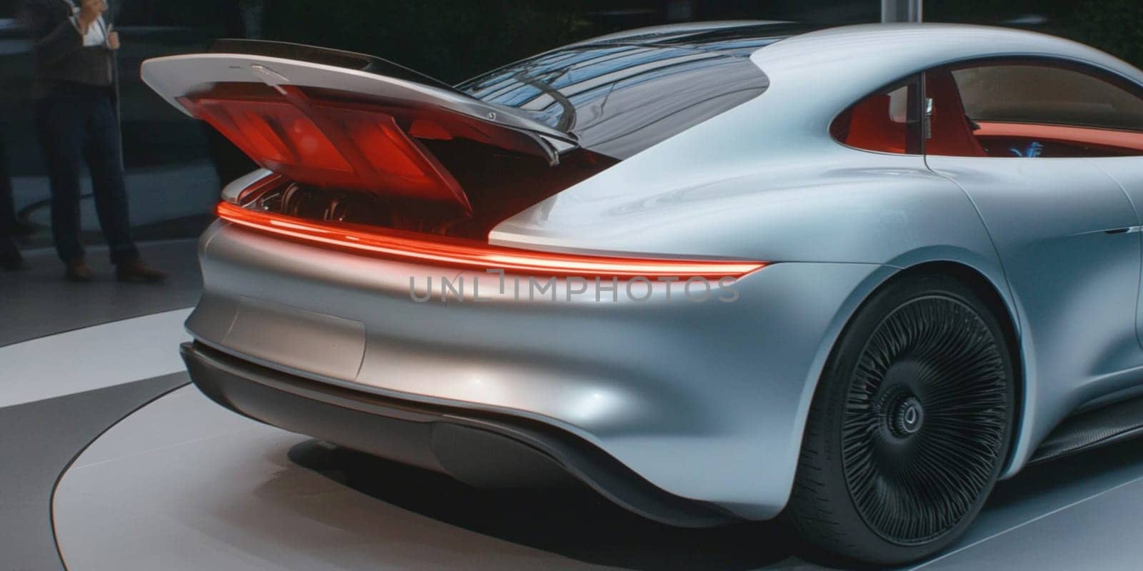 Silver electric sports car is parked in the driveway of a modern, minimalist home. The car is a sleek and stylish design, with smooth curves and sharp angles