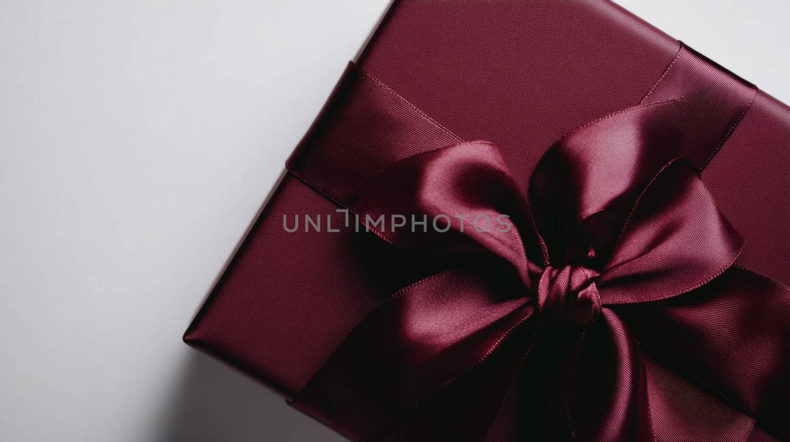 Burgundy gift box with satin ribbon bow, elegant celebration. Luxury gift and festive concept.