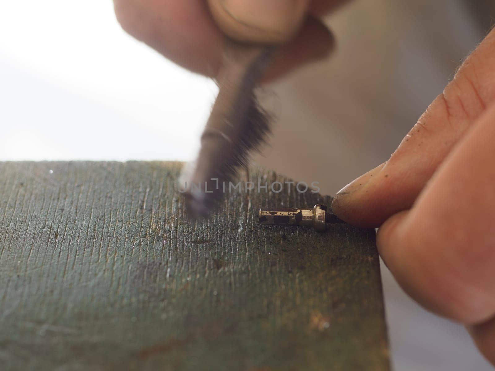 Skilled mechanic cleaning metal part with wire brush in workshop, surrounded by tools. Greasy hands focus on precise craftsmanship. Vintage workbench adds texture
