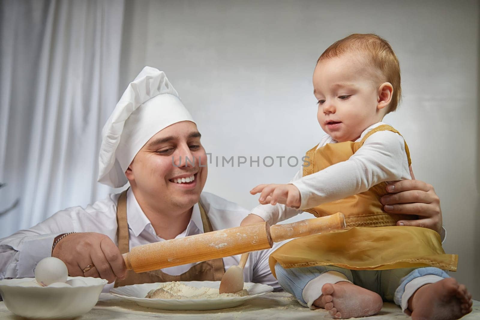 A family enjoys a fun cooking session, playfully covered in flour while engaging with their little ones in a warm kitchen. Father and son having fun