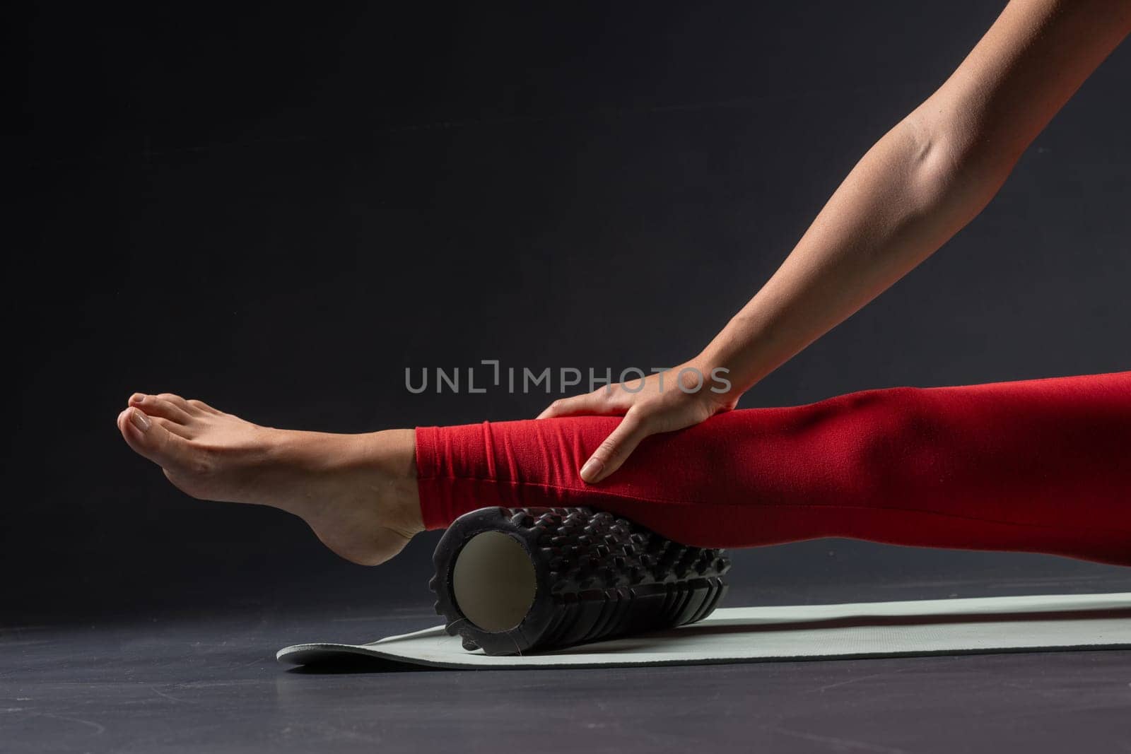 physiotherapy massage, woman with yoga roller on floor for leg tension on dark background, self massage with roller