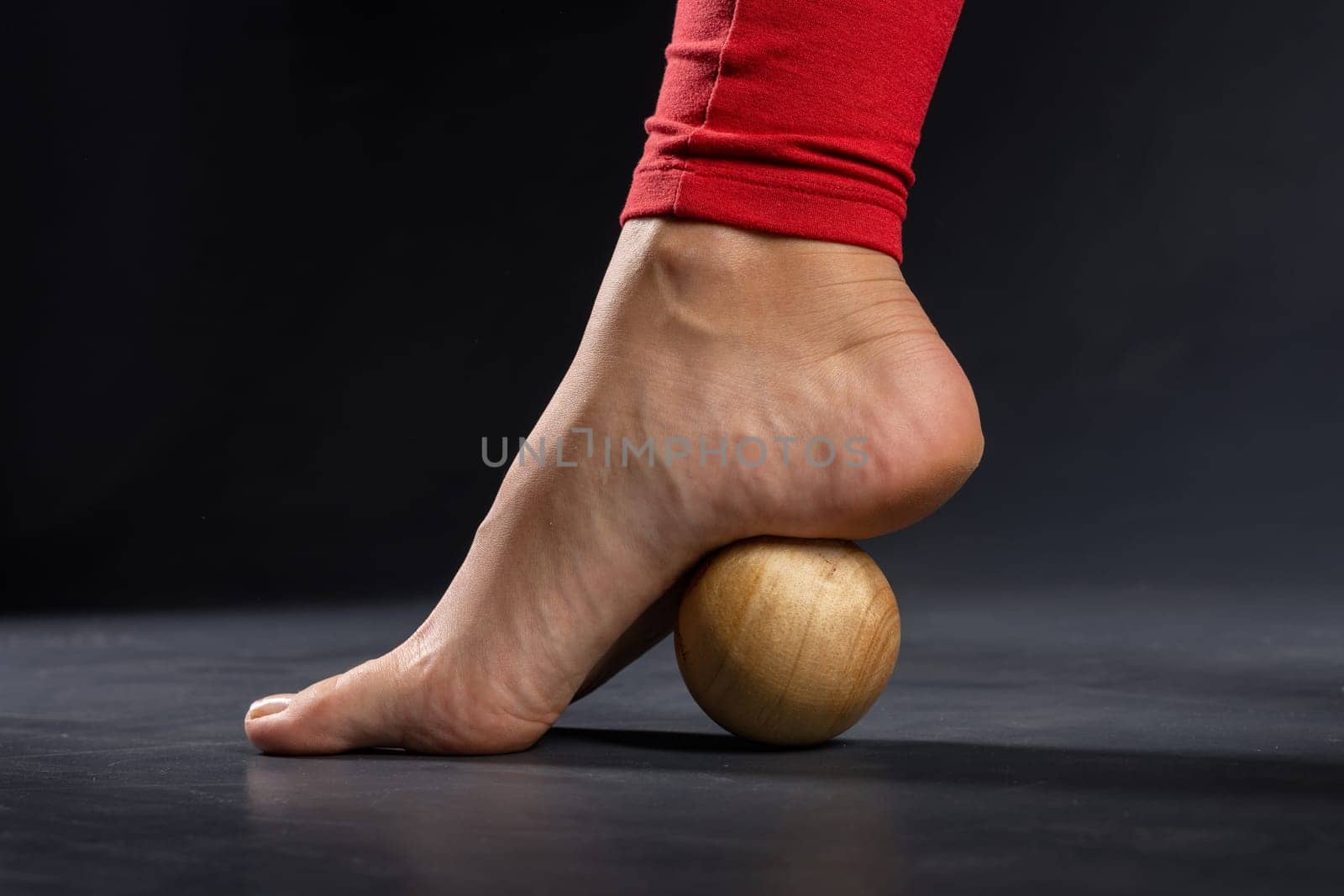 Myofascial release of foot muscles with a massage ball on a dark background, close-up. Concept on the topic of preventing foot fatigue after wearing high-heeled shoes.