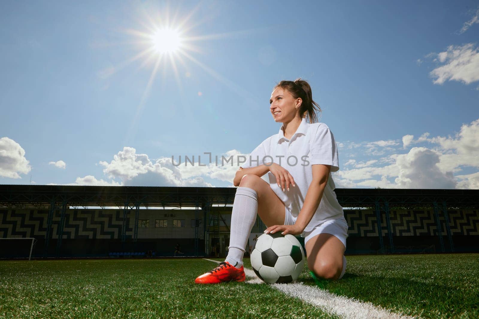 girl Football player in white shorts and red boots standing with soccer ball on green artificial turf field. women football concept