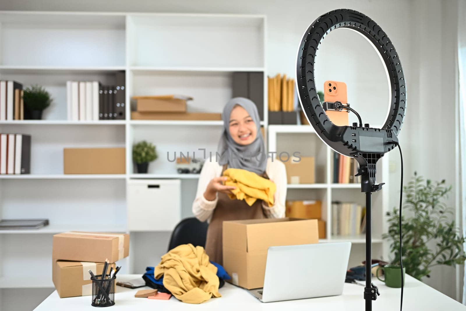 Asian muslim woman in hijab broadcasting live video for selling clothes online at home.