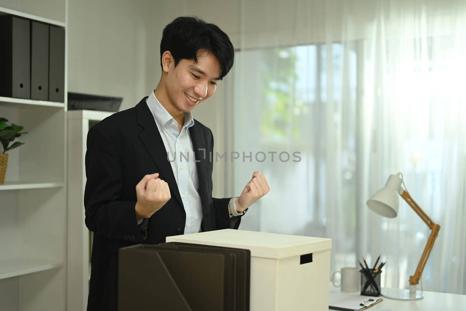 Happy asian male office worker with box of his belongings moving into a new office.