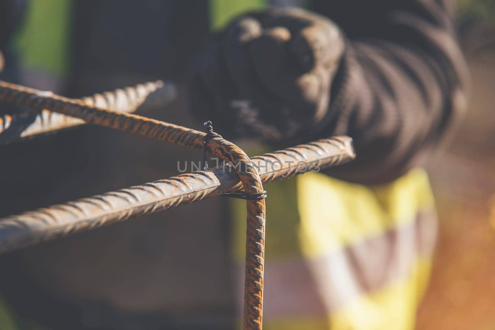 A worker uses steel tying wire to fasten steel rods to reinforcement bars close-up. Reinforced concrete structures - making a steel reinforcing cage for concrete beam
