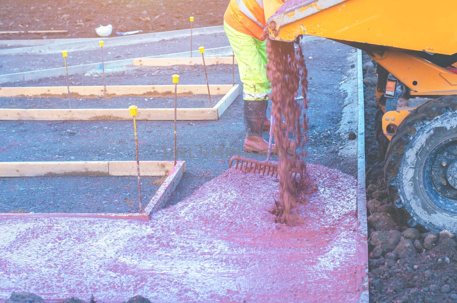 Builders pouring and levelling wet ready-mix concrete into formwork   during new footpath construction
