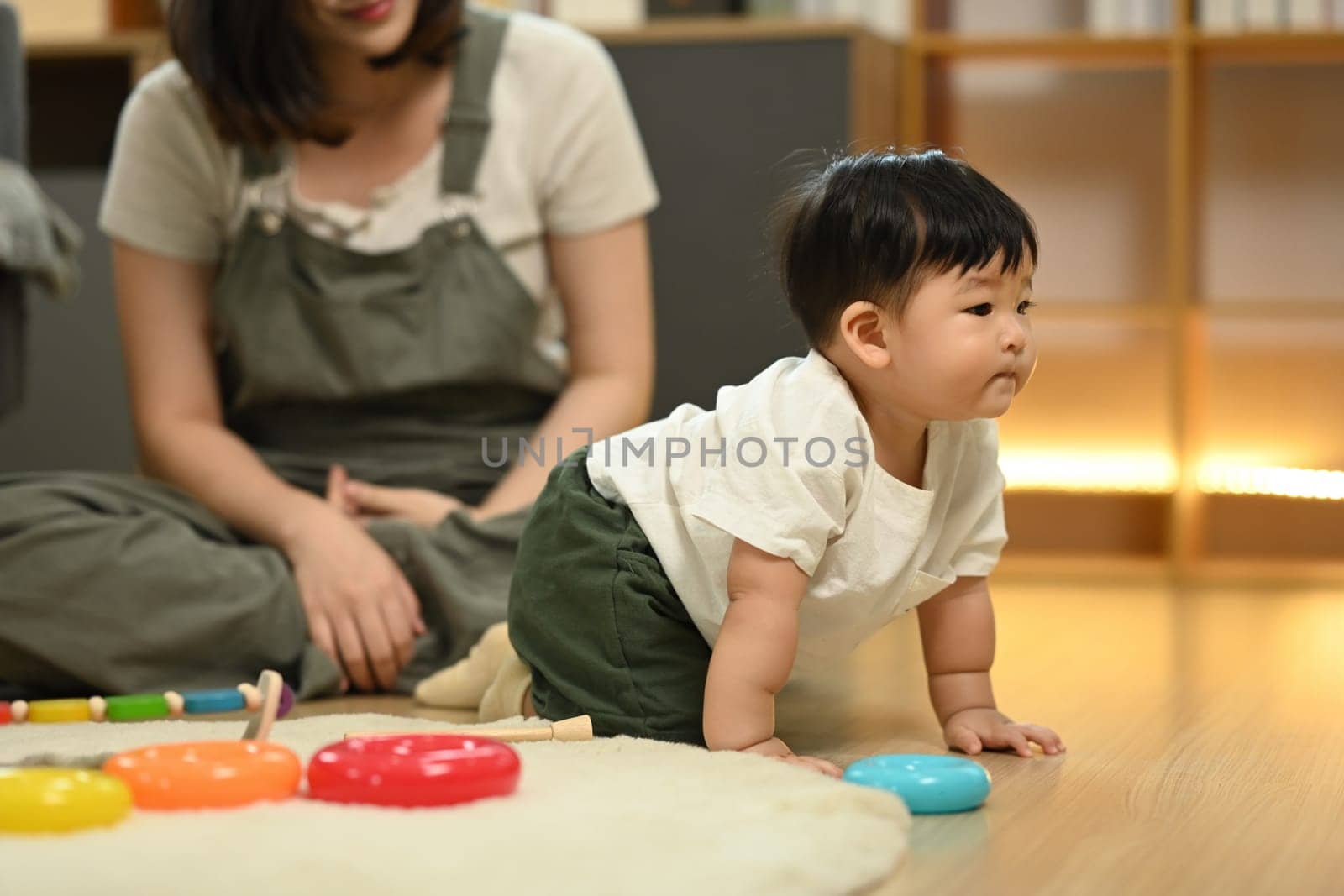 Little baby boy learning to crawl with supportive mother closely watching from behind. Childhood and development concept.