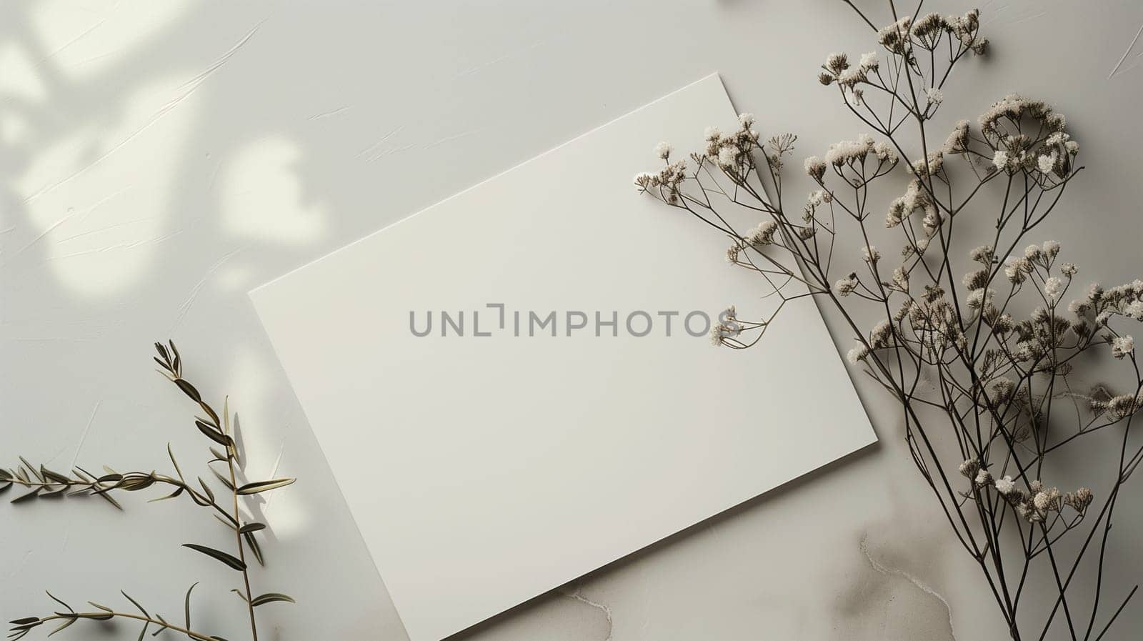 A blank white canvas lies on a light-colored surface, bordered by delicate dried flowers and soft greenery. The natural arrangement highlights the simplicity and elegance of the scene, inviting creativity.