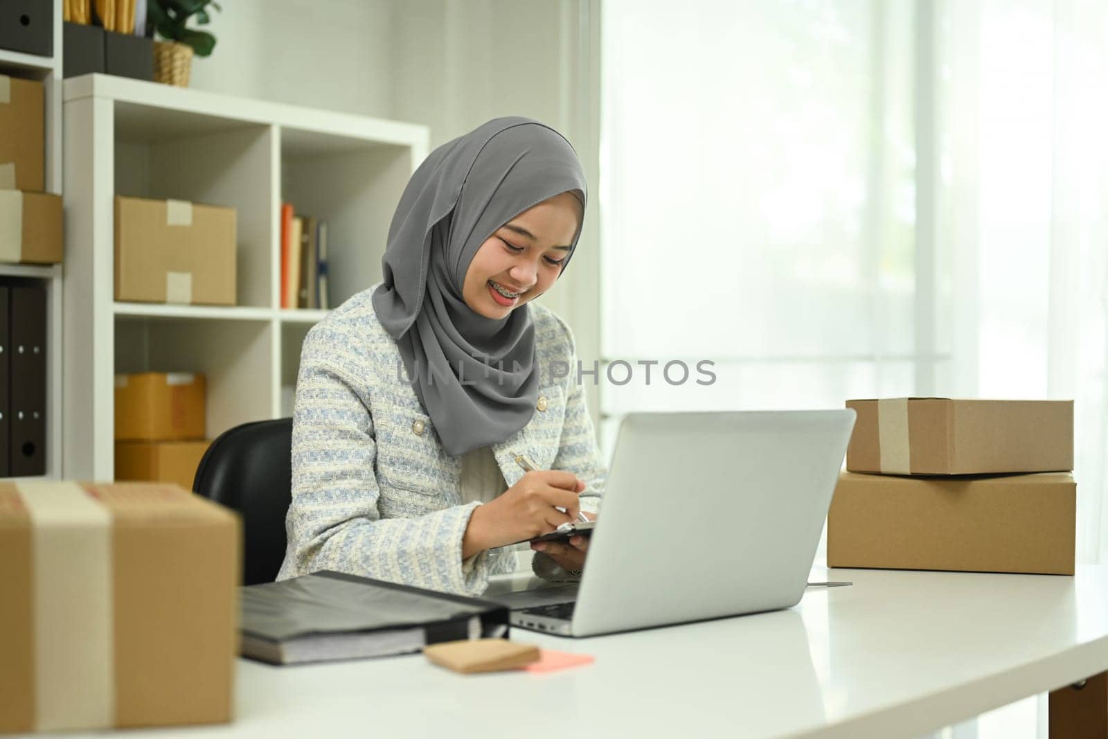 Young Muslim woman managing online store working on laptop at home office.