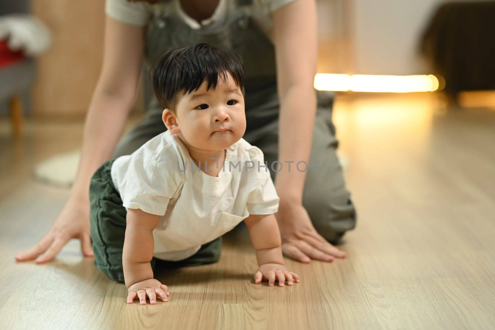 Little baby boy learning to crawl with supportive mother closely watching from behind. Childhood and development concept.