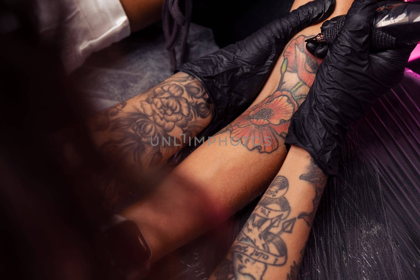 Professional tattoo master in black rubber gloves creating colorful artistic masterpiece on female client arm in parlor, cropped shot