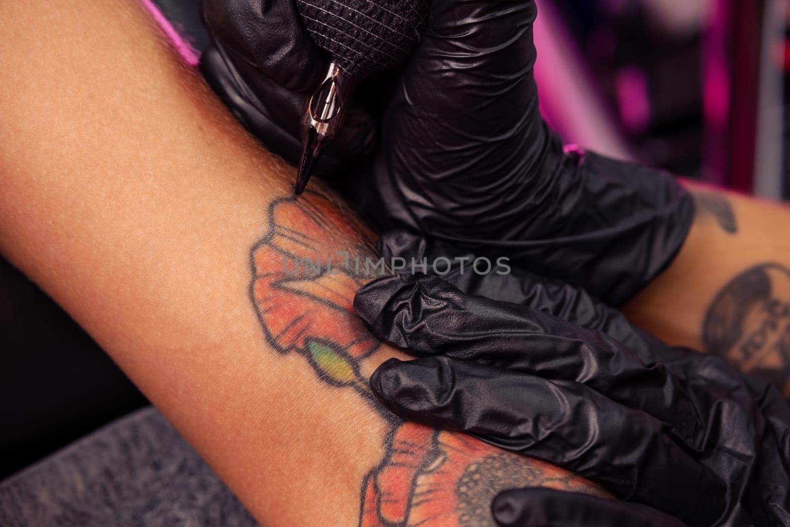 Closeup image showing precision and artistry of creating colorful poppies tattoo on female arm. Professional master using ink tattooing machine