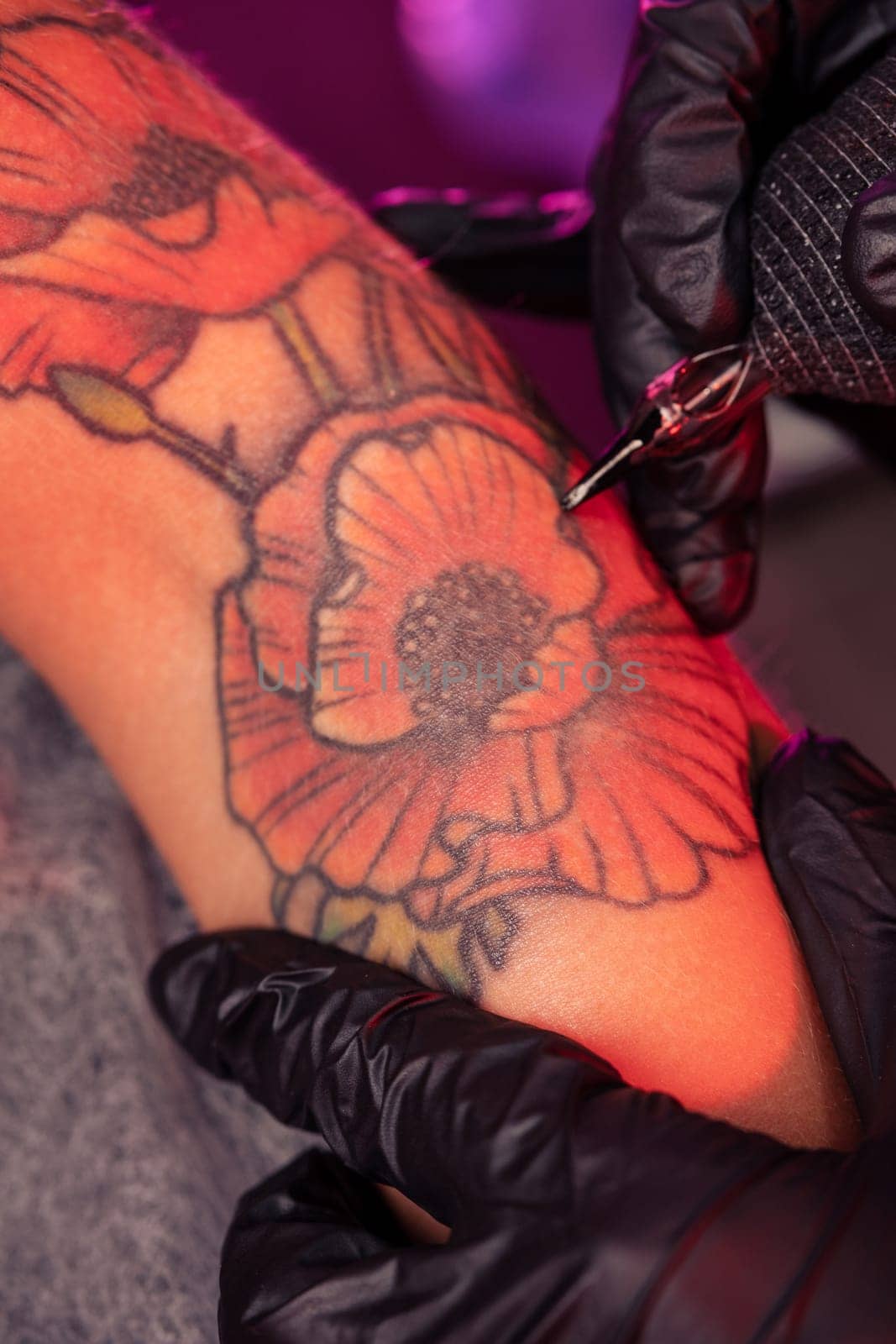 Closeup of creation of bright colorful poppies tattoo on female hand with professional tattooing device