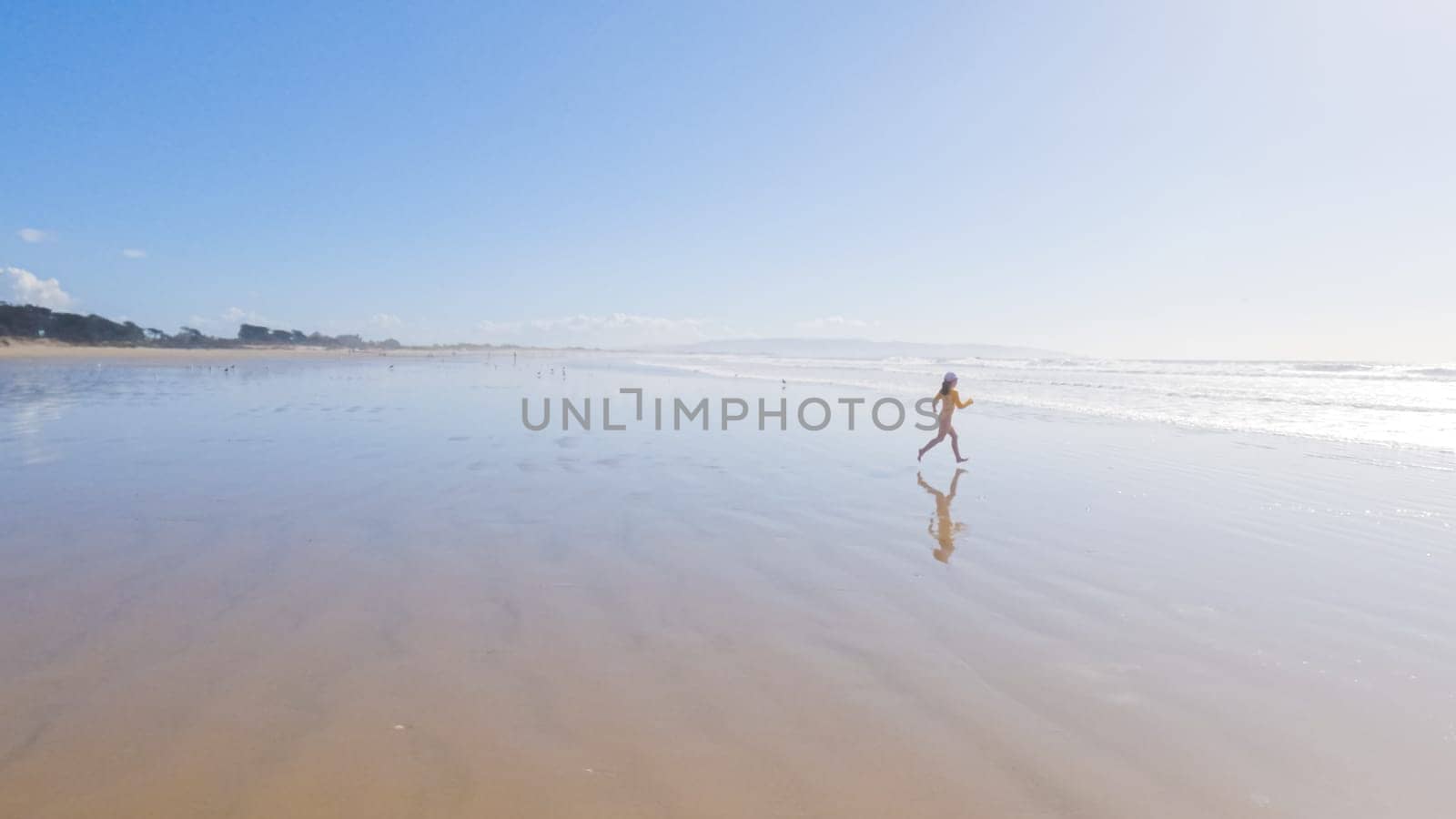 Little girl, braving the cold, joyfully runs in her swimsuit across the beach during winter.