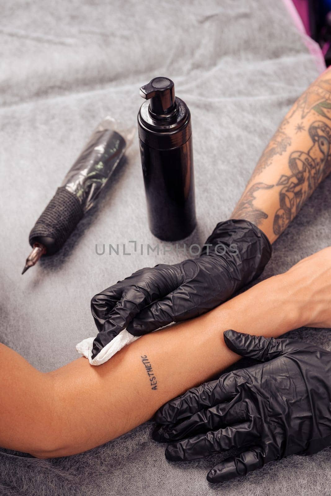 Professional skillful tattoo artist treating and cleansing tattooed skin on female arm with antibacterial foam, cropped shot