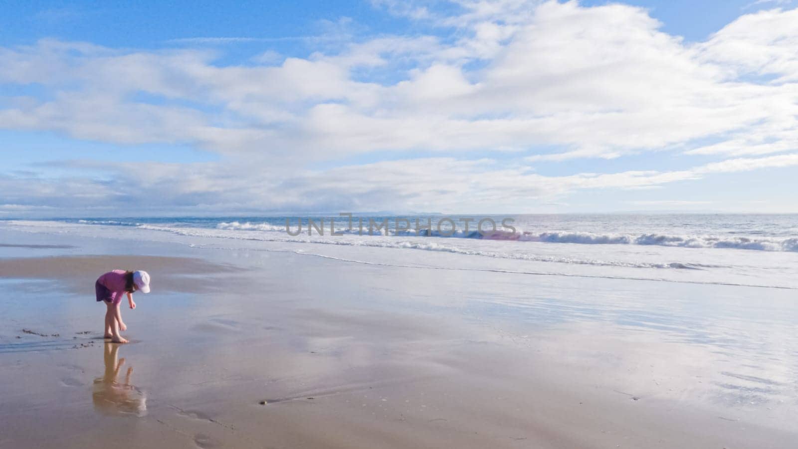 A little girl joyfully plays on the vast, empty sands of El Capitan State Beach in California during winter.