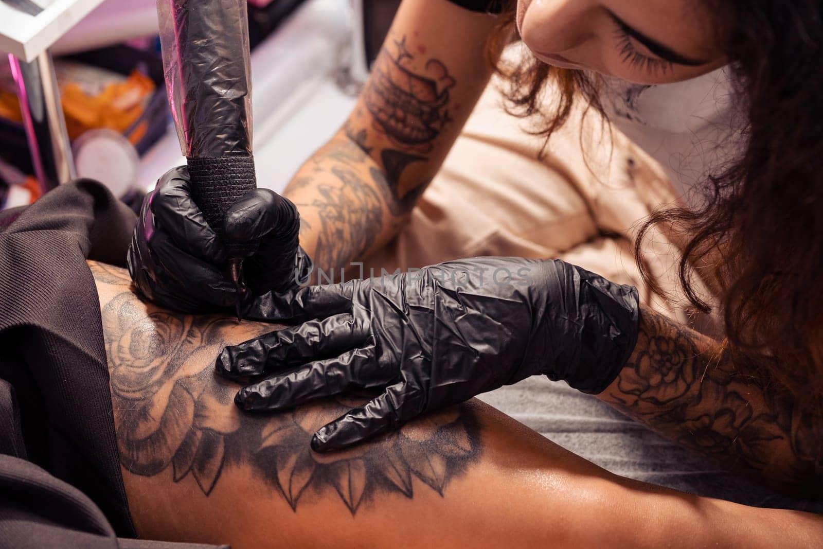 Professional tattooist with focused attention creating black and white flower design on thigh of female client, using tattoo machine