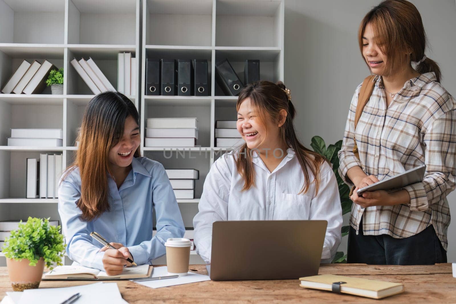 Asian College groups of students using laptop, tablet, studying together with notebooks documents paper for report near windows in classroom. Happy young study for school assignment, Soft focus by wichayada