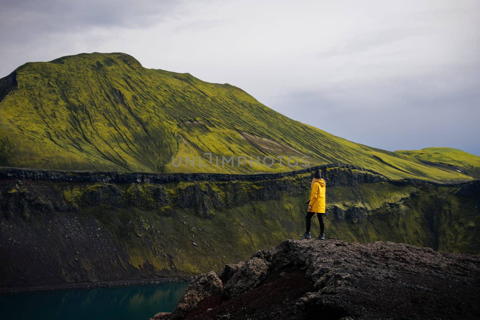 This photo shows a backpacker girl taking in the view of Blahylur lake in Iceland. She is standing on the shore of the lake, looking out at the surrounding mountains and glaciers. The sky is cloudy, creating a sense of drama and suspense. This photo is perfect for use in travel and nature photography. It could be used to illustrate a story about the beauty of Iceland, or it could simply be used to create a sense of awe.