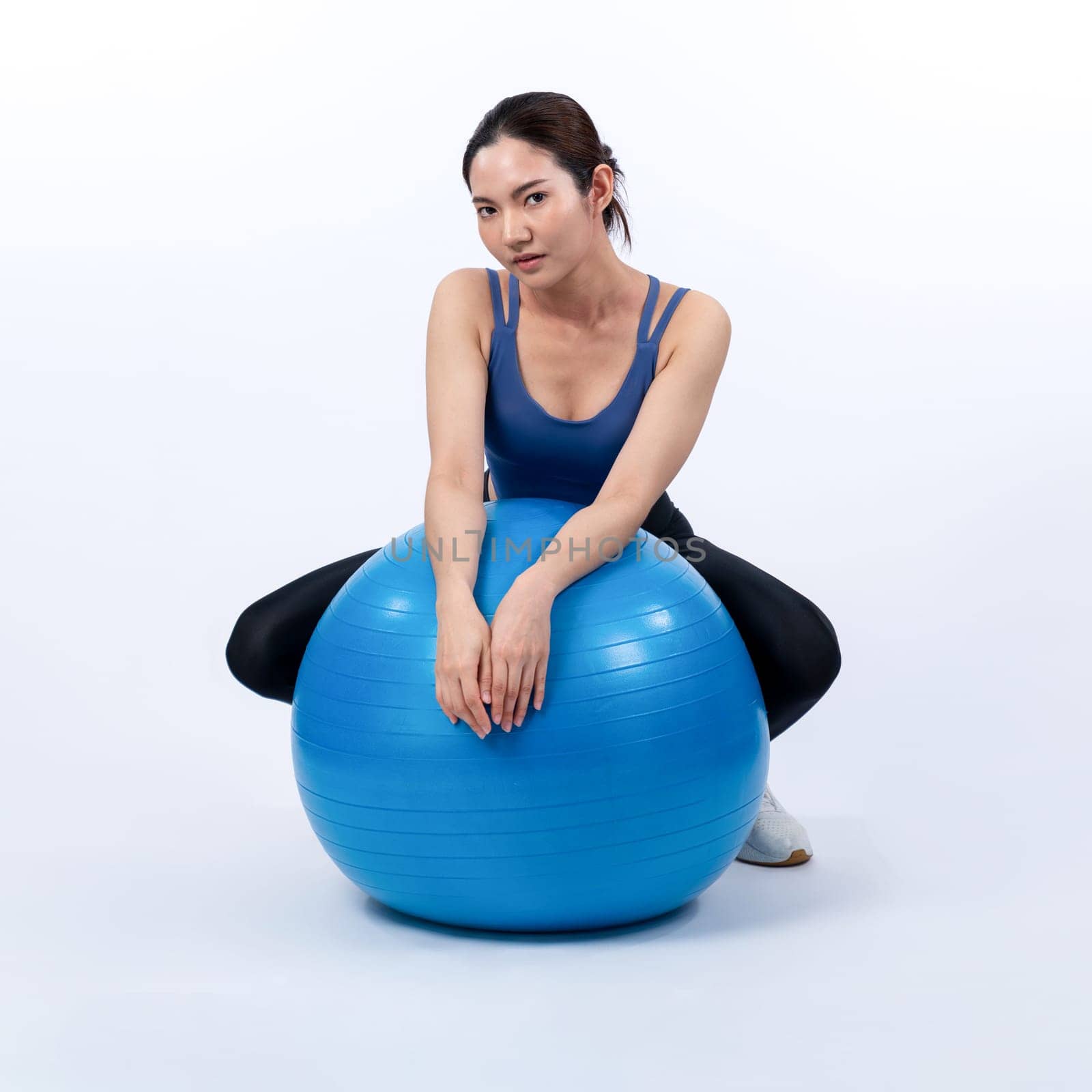 Young attractive asian woman portrait in sportswear with fit ball targeting on abs muscle for effective energetic daily workout routine. Studio shot and isolated background. Vigorous