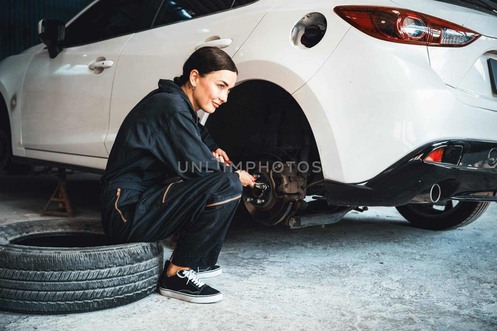 Hardworking female mechanic changing car wheel in auto repair workshop. Oxus by biancoblue