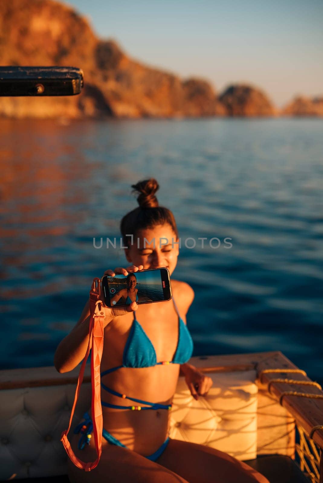 A young woman finds joy in the beautiful sunset as she relaxes on a boat, capturing precious memories with her camera