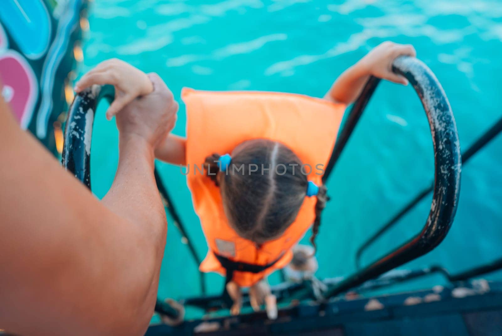 A young child, wearing a bright orange life vest, confidently climbs a tall ladder, excited for their water adventure