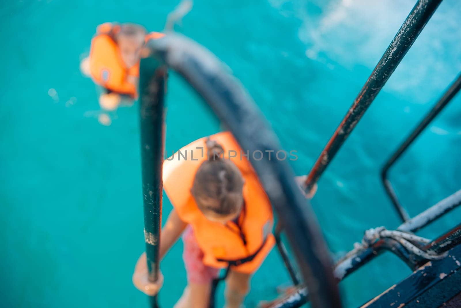 Two individuals climbing a ladder into turquoise waters, wearing life jackets for safety and protection