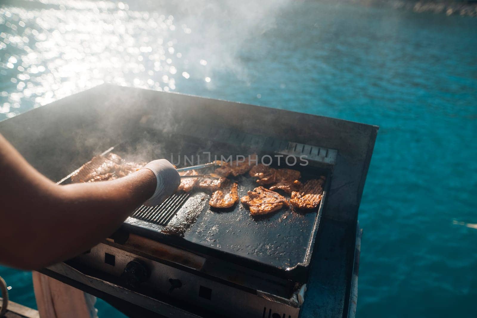 A skilled chef expertly grills a variety of fresh seafood on a portable grill beside stunning blue waters