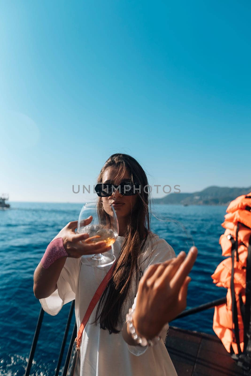 A woman unwinds on a boat with a refreshing drink, fully embracing the carefree and joyous summer vibes by the ocean