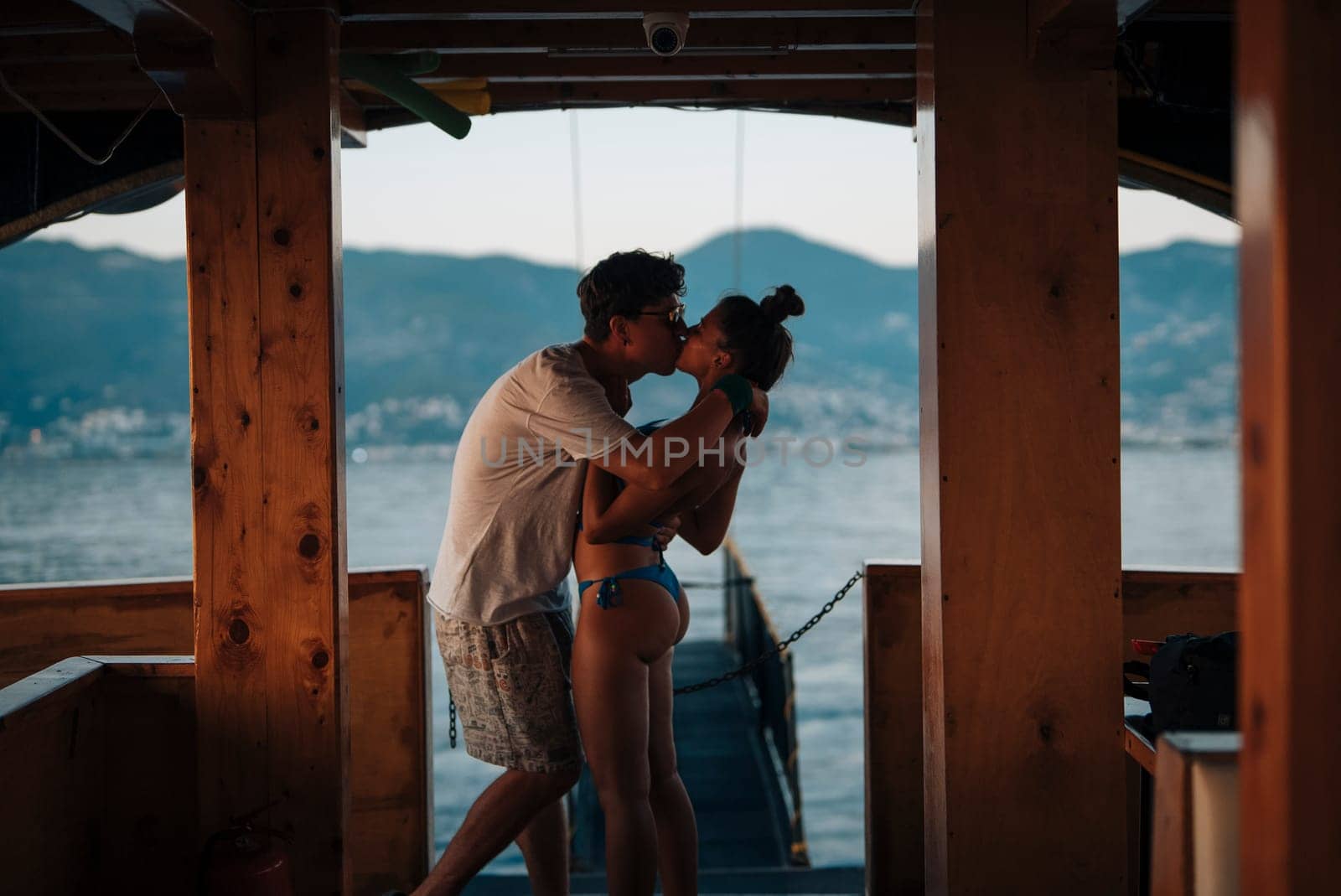 A romantic couple is sharing a passionate kiss while on a boat, set against the backdrop of a beautiful sunset