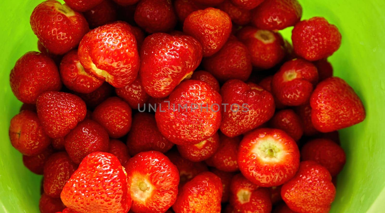 Sun-kissed strawberries, freshly picked and arranged beautifully, sit in a vibrant green bowl, radiating summer's warmth