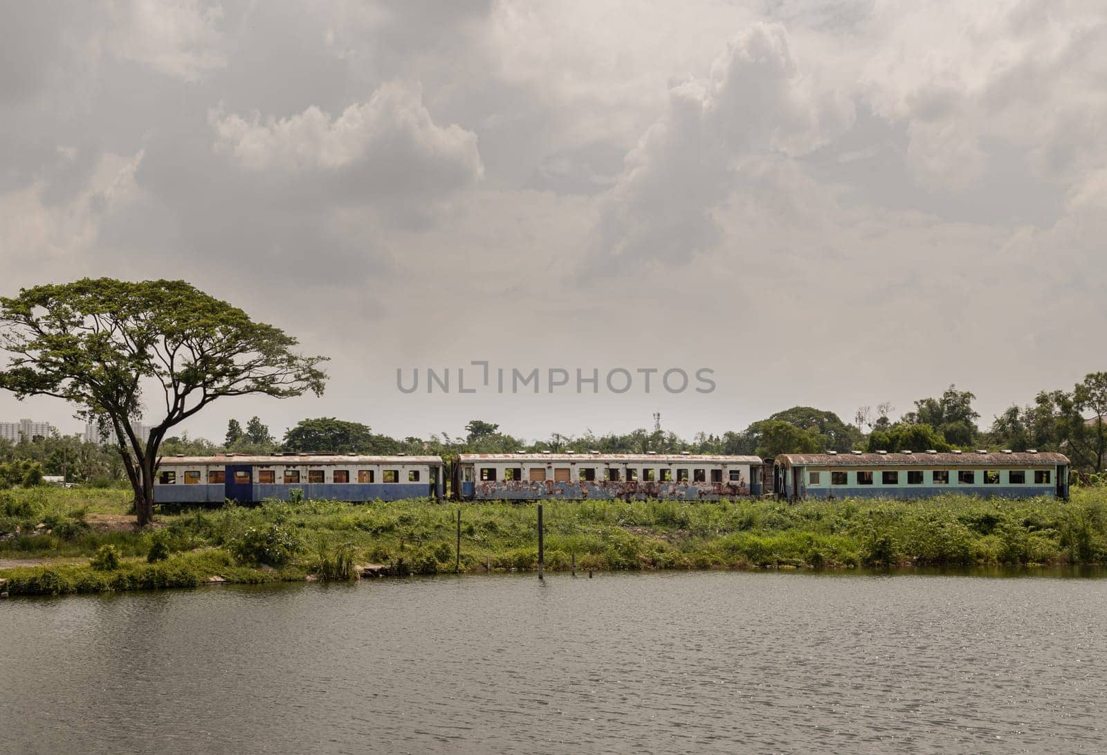 Bangkok, Thailand - May 28,2022 - View of vintage railroad container is parked in wasteland and swamp with sky background. The empty old rusty passenger train and abandoned, Space for text, Selective focus.